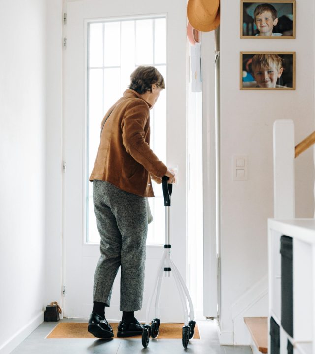 An elderly woman using a rollator to exit her home, capturing daily life.